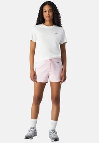 Hvid kortærmet t-shirt med lille logo, parret med lyserøde shorts med elastisk talje og snøre, båret med atletiske sko.