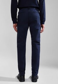 Pantaloni blu navy in cotone, caratterizzati da una vestibilità slim, passanti per cintura e due tasche posteriori; indossati con scarpe nere.