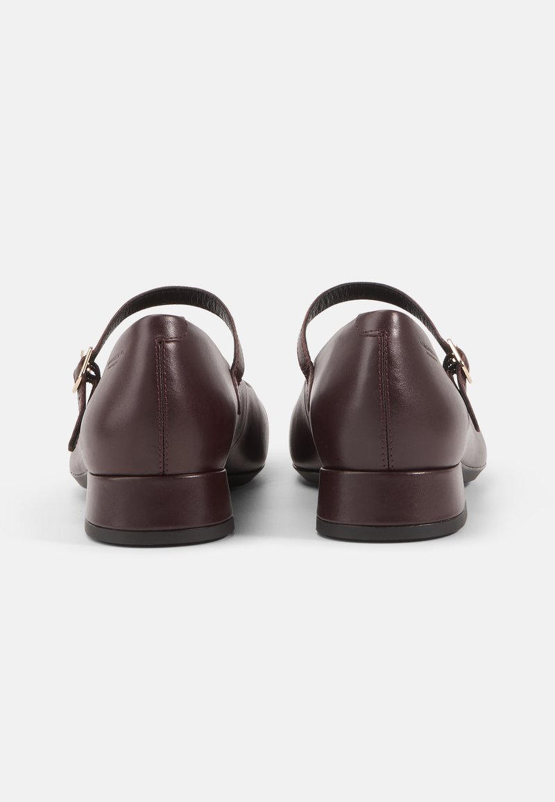 Bruna läderskor med låg klack, som har en bakrem och detaljer i guldmetall. Slät textur och rund tåkonstruktion.