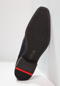 Navy leather shoe with a textured black rubber sole, featuring a red accent strip and geometric pattern on the bottom for grip.