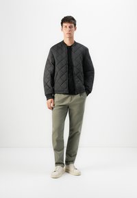 Must mustriga bomber-jakk mustas, millel on soonikuga varrukad, kantud musta särgi peale. Ühendatud helesiniste pükstega ja valgete tossudega. Minimalistlik disain.
