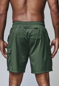 Grøn cargo shorts har justerbar talje, sidelommer og en lynlåslomme bagpå. Glat stof med en let struktureret overflade.