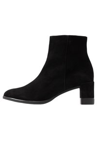 Bottine en suède noir avec un bout arrondi et un talon bloc de taille moyenne. La bottine présente une texture lisse et des côtés sans couture.