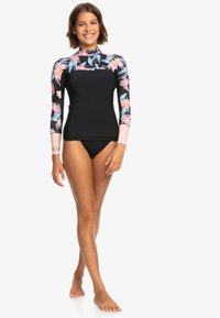 Top de neopreno negro para mujer con mangas largas de flores en rosa, azul y verde. Incluye cuello alto y detalle de logo en la muñeca.