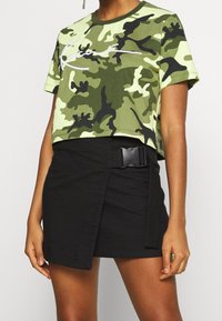 Krótkotop w kamuflażu w odcieniach zieleni z białą grafiką, zestawiony z czarną, teksturowaną spódnicą o fasonie wrap z bocznym zapięciem na klamrę.