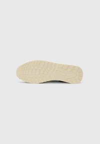 Schuhsohle mit einem strukturierten Gummimuster in Cremefarbe, tiefen Profilen und erhöhten Akzenten für Grip und Traktion.
