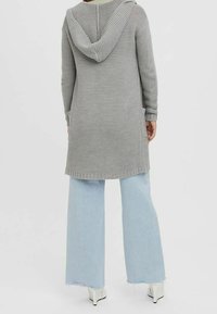 Šedý pletený cardigan s kapucí, s žebrovanými manžetami a lemem, nošený přes světle modré široké džíny a bílé lodičky na vysokém podpatku.