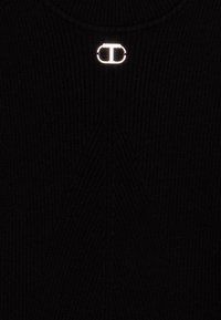 Pull noir côtelé avec un col haut et un accent logo argenté au niveau du col, affichant une surface texturée avec des lignes verticales.