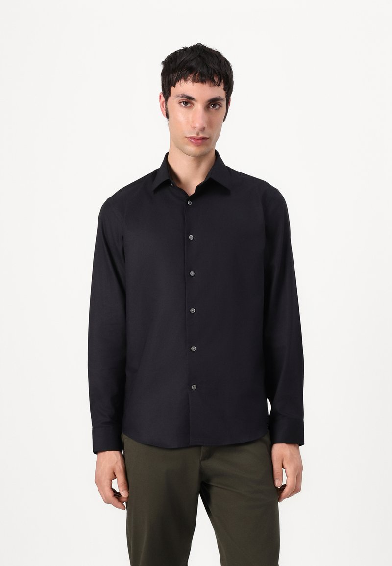 Black long-sleeve shirt featuring a button-down front, classic collar, and smooth texture, worn with olive green pants.
