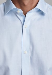Jasnoniebieska koszula z guzikami wykonana z gładkiego, lekkiego materiału. Posiada kołnierzyk rozłożysty oraz dwa białe guziki na przodzie.