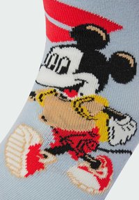 Calcetines de color azul claro con un diseño de dibujos animados tejido y colorido de un personaje que lleva una gorra y zapatos rojos, con acentos en amarillo y negro.