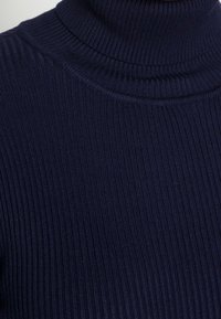 Pull à col roulé côtelé bleu marine avec textures verticales et coupe ajustée, mettant en valeur la chaleur et le confort grâce à son tissu.