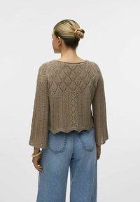 Maglione lavorato a maglia in taupe con design a rete aperta e maniche a campana a tre quarti. Abbinato a jeans in denim blu a vita alta.