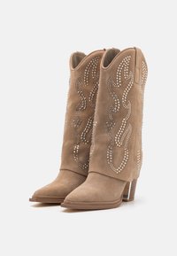 Botas de vaquero de ante beige con punta afilada, adornadas con rhinestones en un patrón de llamas y con tacón apilado.