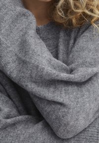 Pull gris en maille avec une finition douce et texturée, coupe ample, présentant un col côtelé et des manches drapées.