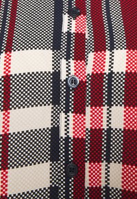 Camicia button-up con un motivo a quadri rosso, nero e bianco, realizzata in un tessuto testurizzato e con bottoni neri. Design a griglia caratteristico con quadrati alternati.