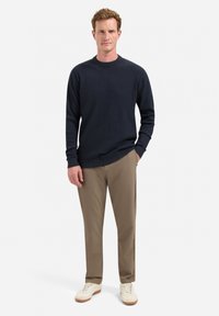 Marineblauwe geribde trui met een ronde hals, gecombineerd met beige broek en witte sneakers. De outfit heeft een textuur gebreide ontwerp.