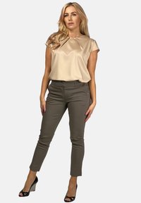 Beżowa bluzka z plisowanym przodem, zestawiona z wąskimi oliwkowymi spodniami. Czarnie sandały na grubych obcasach dodają wysokości. Neutralna paleta kolorów.