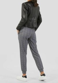 Giacca in pelle nera corta, pantaloni grigi a fantasia con polsini elasticizzati e sneakers bianche con accenti neri; mostrato da un angolo posteriore.