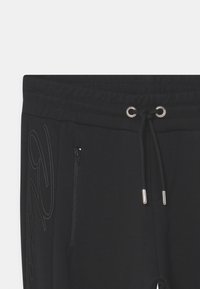 Zwarte joggingsbroek van zachte stof, met een elastische tailleband met trekkoord, zijzakken met rits en een bijpassend logo-detail.