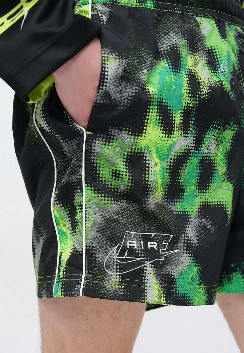 Black shorts with a green and gray dotted pattern, featuring white piping and a printed "AIR" logo by Nike on the lower leg.