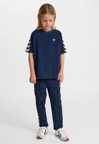 Maglietta di cotone blu navy con scollo rotondo e tre strisce bianche a forma di chevron su ogni manica. Abbinata a pantaloni blu navy coordinati.