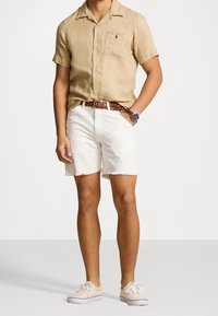Camisa de lino de manga corta color marrón claro, pantalones cortos de mezclilla blancos con dobladillo deshilachado, cinturón de tejido marrón y zapatos de lona beige. Diseño minimalista.