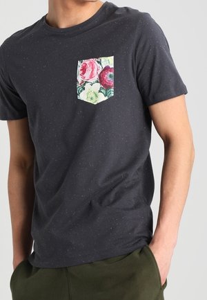 Dark navy t-shirt with a speckled pattern, featuring a floral patch pocket in pink and green hues. Short sleeves and a crew neckline.