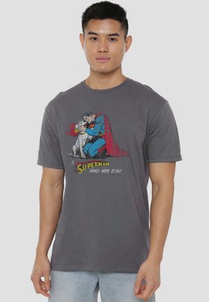 Young man wearing gray t-shirt with graphic of Superman kneeling and hugging a white dog, text "Superman and his dog."
