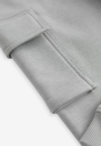 Tessuto di felpa grigia, texture liscia, con orlo della manica ripiegato e dettagli di cuciture rinforzate. Design minimalista senza motivi.