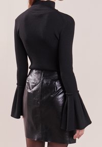 Zwarte geribbelde coltrui met uitlopende manchetten, gecombineerd met een glanzende zwarte leren minirok. Soepele textuur en aansluitend ontwerp.