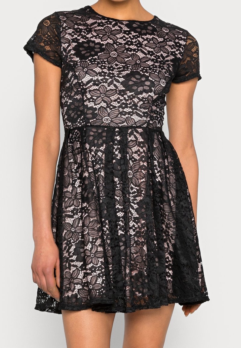 Robe en dentelle noire avec un motif floral, à manches courtes et à corsage ajusté. La jupe a une forme évasée et des détails en dentelle texturée.