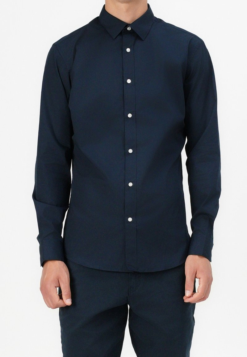 Camicia a maniche lunghe blu navy realizzata in tessuto morbido, con colletto a punta, chiusura con bottoni e bottoni argentati sulla patta.