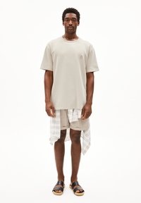 Lichtgrijs katoen t-shirt, losse pasvorm; beige shorts met een klein zakje; wit-blauw geruit shirt om de taille geknoopt; zwarte sliders.