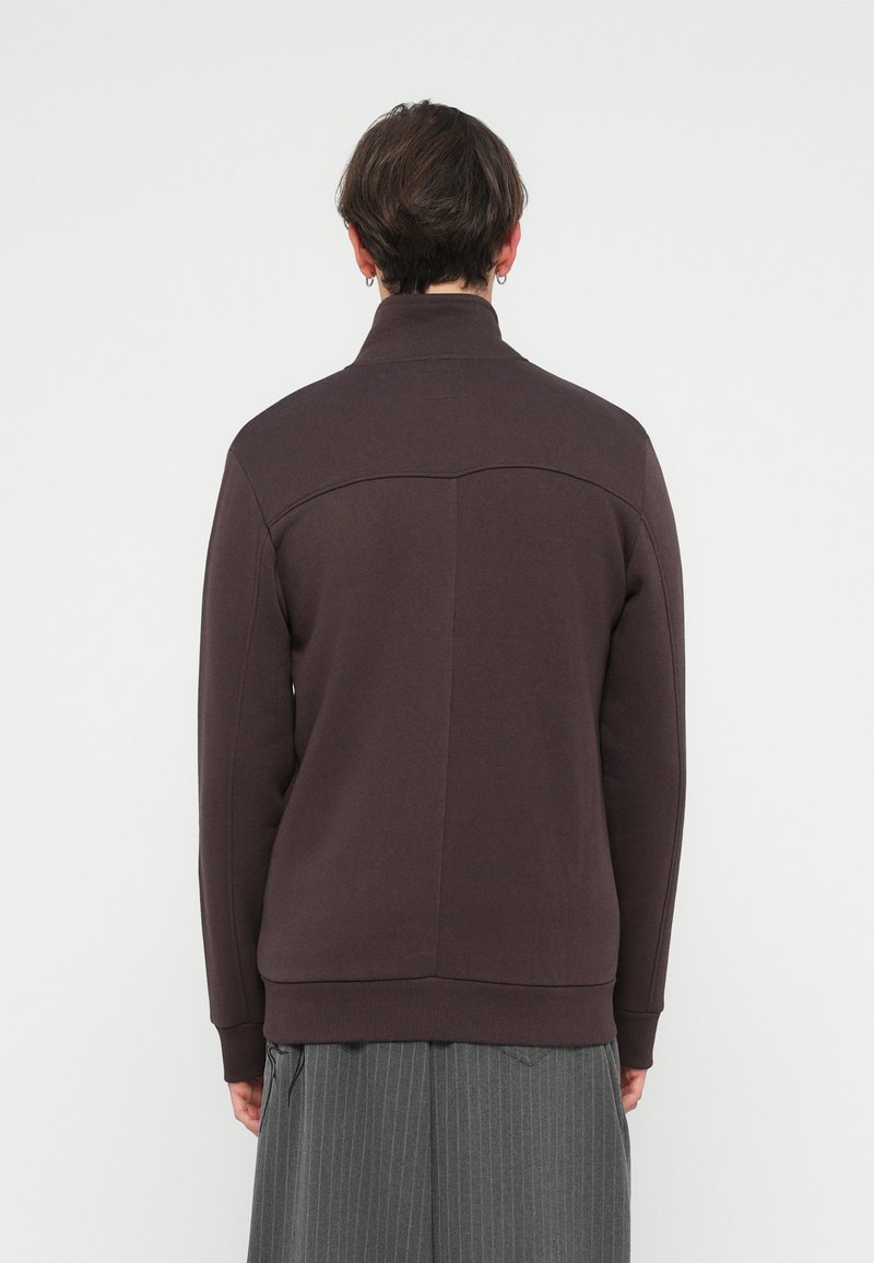 Brun zip-up sweatshirt med høj krave, ribbede manchetter og tekstureret stof. Har en vandret søm på den øverste ryg.