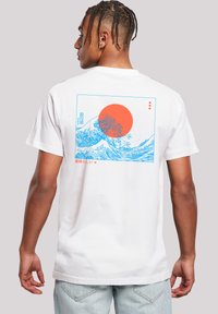 Weißes Baumwoll-T-Shirt mit einem blauen Wellenmotiv und einer orangefarbenen Sonne auf dem Rücken, mit japanischem Text am unteren Rand. Kurze Ärmel.
