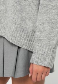 Jasnoszary sweter z dzianiny z ribbowanymi mankietami w połączeniu z szarą spódnicą plisowaną. Miękka tekstura i luźny krój są widoczne w projekcie.