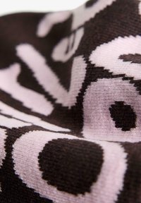 Neulekangas, jossa on musta ja vaaleanpunainen kuvio, suuret pilkut ja abstrakteja muotoja, esittelee pehmeän tekstuurin ja eloisat värit.