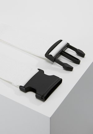 Sangle tissée blanche avec boucle noire en plastique à libération latérale, montrée non attachée sur un coin de surface blanche.