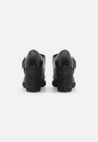 Zapatos de tacón de cuero negro con un diseño de tacón cuadrado. Textura suave y parte trasera redondeada. Acentuados con un detalle de hebilla lateral.