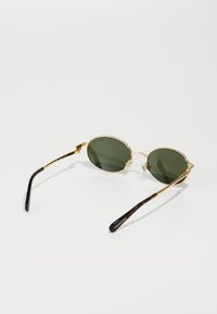 Gafas de sol de metal dorado con lentes ovalados verdes. Presentan almohadillas nasales detalladas y patillas con patrón de carey marrón. Marca grabada en la patilla.