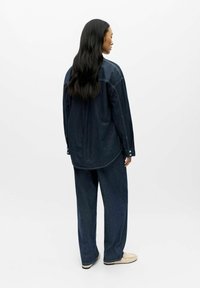 Donker denim shirt en brede pijpen broek, met een ontspannen pasvorm, zichtbare stiksels en knoopdetails. Gladde textuur en diepe blauwe kleur.