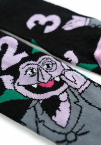 Calze nere con un personaggio vampiro in stile cartone animato, nei toni del viola e del grigio, con accenti rosa e elementi di sfondo verdi.