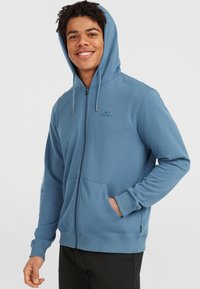 Felpa blu con zip realizzata in tessuto morbido, dotata di tasca a marsupio, cappuccio regolabile con lacci e polsini a coste.