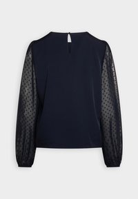 Haut navy avec un corps en tissu uni et des manches transparentes à pois, avec des poignets élastiques et une fermeture à bouton au niveau du col dans le dos.