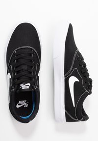 Baskets en toile noire avec accents blancs, bout rond, semelle en caoutchouc blanche et lacets noirs. Présente un logo Nike swoosh blanc proéminent.