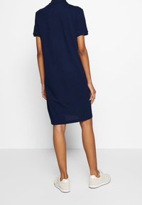 Robe polo bleu marine à manches courtes, coupe légèrement ample et fentes latérales à l'ourlet. Associée à des baskets de couleur claire.