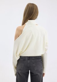 Maglione bianco a coste con design oversize e spalle scoperte. Abbinato a jeans neri a vita alta, con classico stile a cinque tasche.