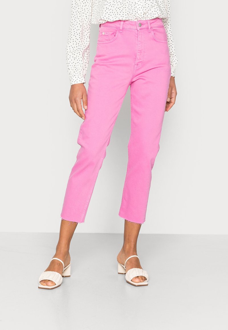 Jeans de mezclilla rosas con cintura alta, largo recortado y dobladillo deshilachado. Combinados con sandalias de tacón cuadrado blancas.