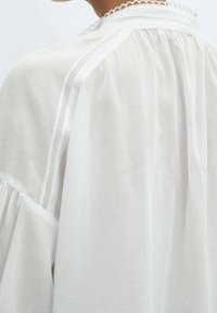 Witte blouse met een ronde, gegolfde halslijn, geplooide details aan de achterkant en zachte, lichte stof met een vloeiende silhoeet.